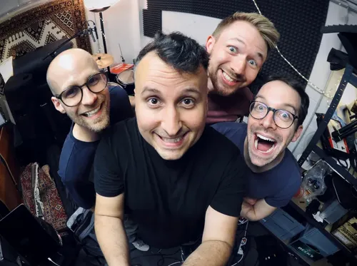 Die vier Mitglieder der Band Givenback lächeln im Proberaum in die Kamera mit einem Fischaugenobjektiv.