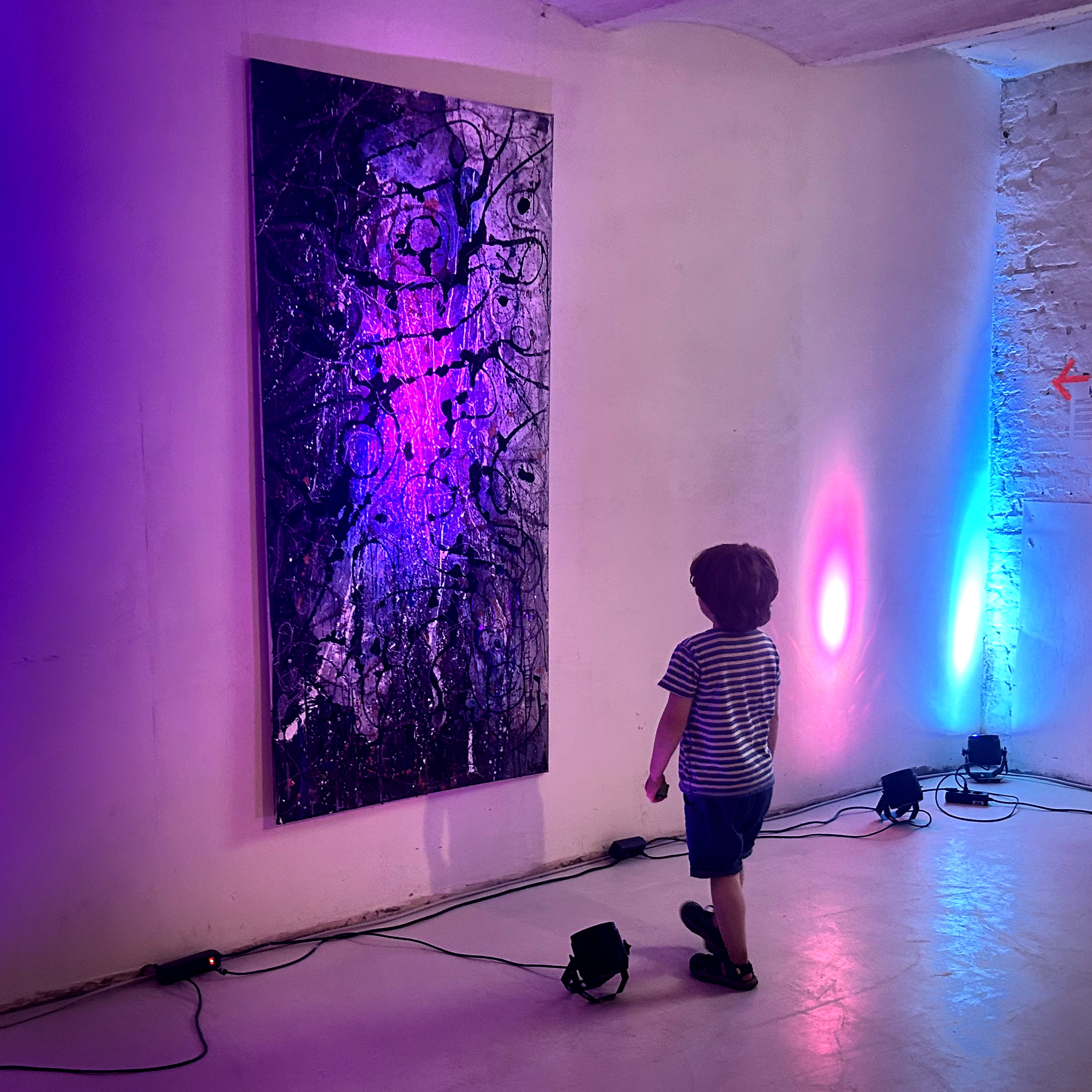 Ein kleines Kind schaut sich eine großes Kunstwerk an einer Wand an.